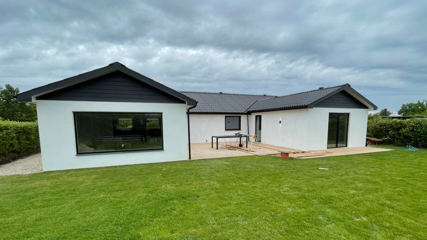 Moderne villa med sort tag, hvide facader, store vinduer og ny træterrasse